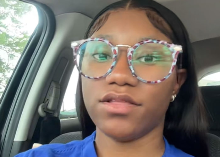 Young woman wearing colorful glasses inside a car, representing concerned US teachers warning about literacy crisis.