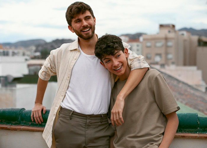 Two brothers on a rooftop, smiling and embracing, representing a teen working two jobs to survive after losing parents.