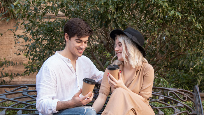 Teen holding coffee with woman on bench outdoors, reflecting struggle of teen losing parents and working two jobs.