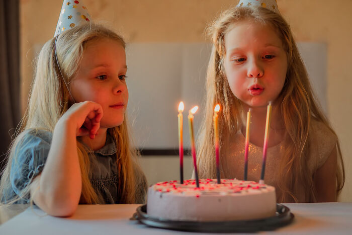 Two young girls wearing party hats, one blowing out candles on a birthday cake, highlighting normal people's habits. - 34