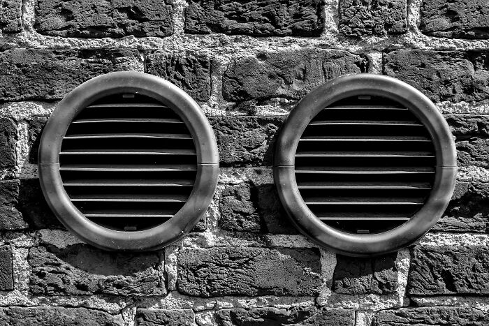 Two round black vents on a textured brick wall symbolizing Singapore experienced mass panic and unusual facts.