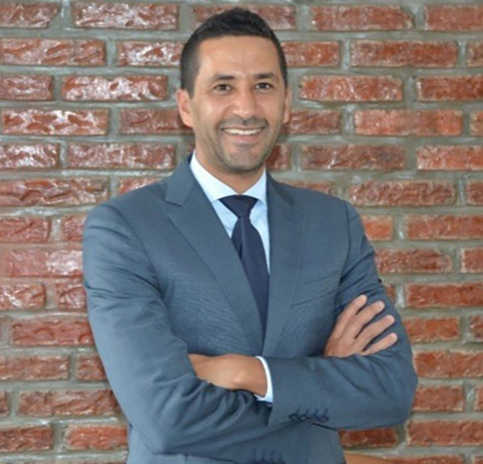 Man in a gray suit standing with arms crossed against brick wall, related to police inconsistencies in missing girl case. - 4