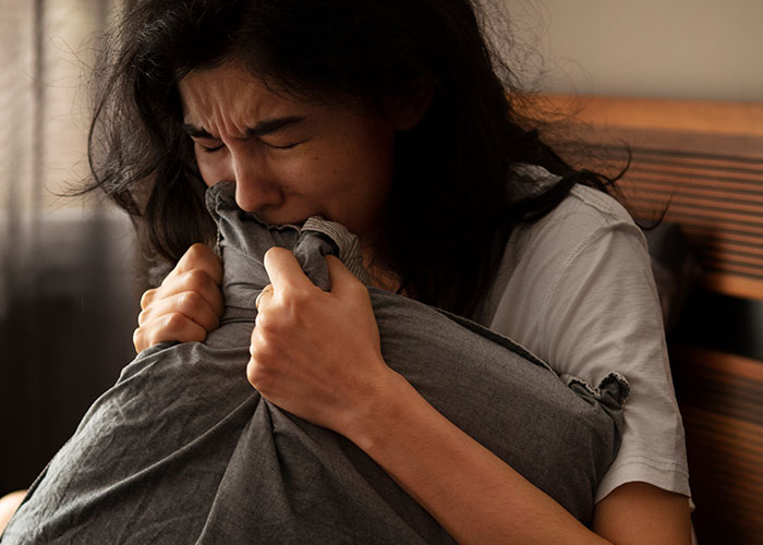 Woman showing distress and fear, clutching a pillow tightly, illustrating quick thinking in a dangerous situation.