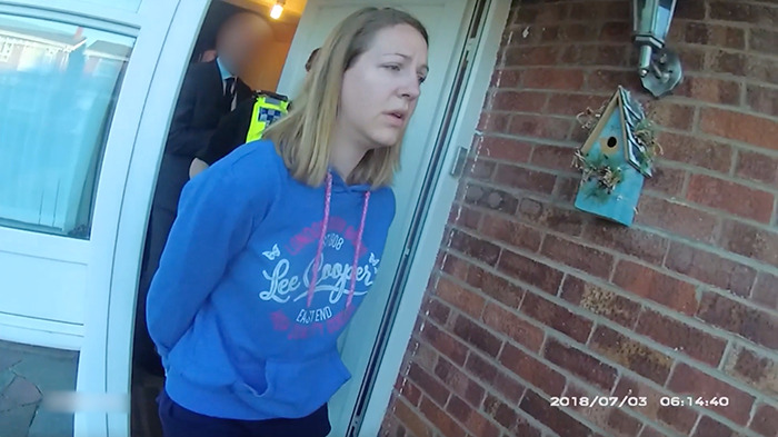 Woman in blue hoodie being escorted by police officers outside a brick house in police arrest over foul play suspicions. Woman in blue hoodie being escorted by police officers outside a brick house in police arrest over foul play suspicions.