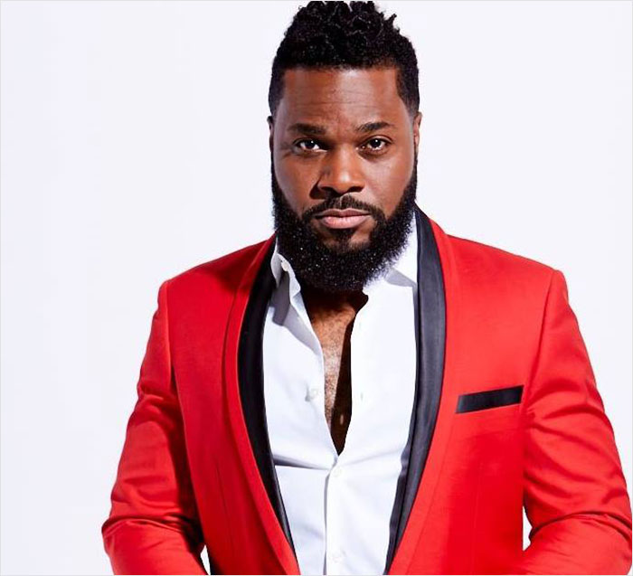 Malcolm-Jamal Warner in a red jacket and white shirt, posing confidently in a studio setting amid public mourning. - 2