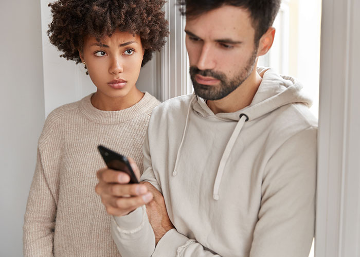 Young man looking at his phone while woman appears upset, illustrating the man calls his girlfriend sister situation.