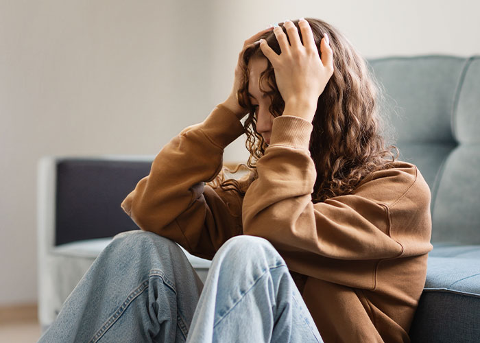 Young woman sitting on the floor with hands on her head, feeling stressed after man calls his girlfriend sister.