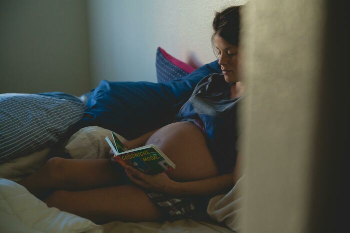 Pregnant woman reading a book in bed, highlighting tension with guy fed up with pregnant roomie situation. - 1