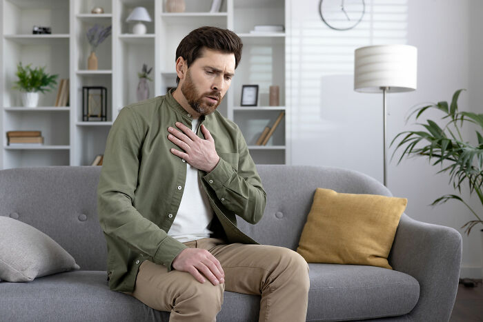 Man sitting on a sofa clutching his chest, appearing unwell, illustrating impostor patients needing less meds and common sense.