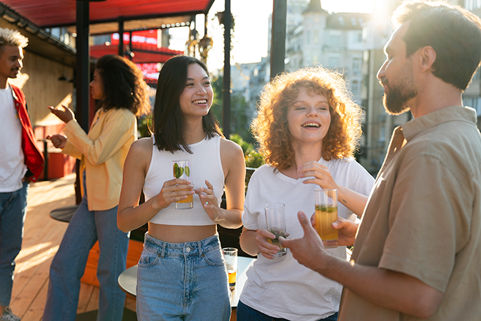 Group of young adults socializing outdoors with drinks, capturing a playful flirty bachelor vibe after public demotion to friend.