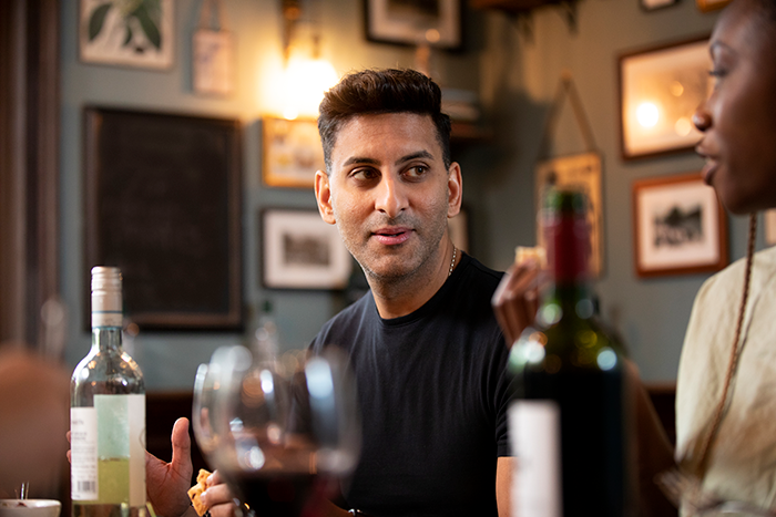 Man in black shirt confidently socializing at a bar, embodying flirty bachelor vibes after public demotion by girlfriend.