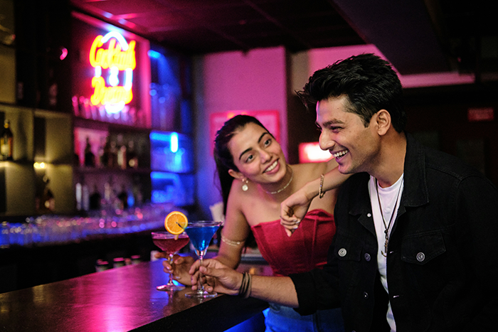 Man flirting with woman at a bar, enjoying drinks and lively conversation in a social nightlife setting.