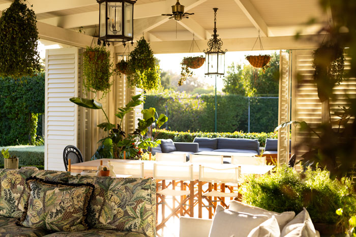 Man relaxing on a patio surrounded by lush plants and cozy seating in a bright, sunlit outdoor space.