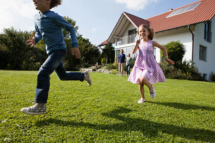 Children running on a green lawn outside a house, illustrating man banning children from his property due to entitled parent. - 1