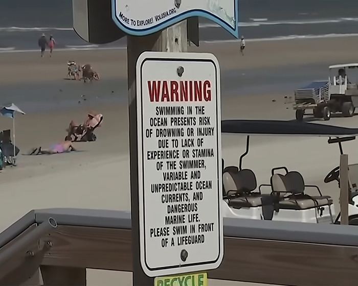 Warning sign at beach about ocean risks and dangerous marine life near Florida where surfer was headbutted by flying shark.