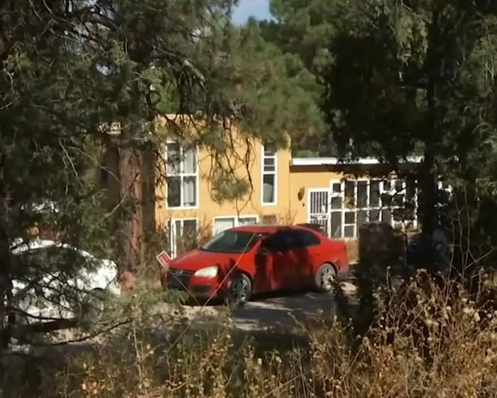 Red car parked in front of a yellow house surrounded by trees in a scene related to family crime investigation.