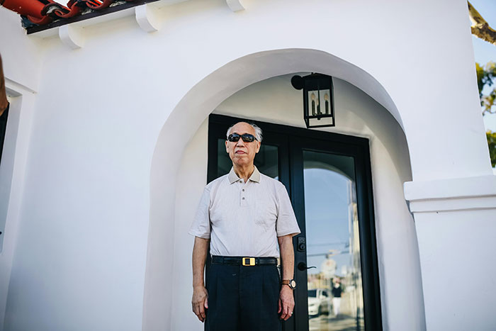 Elderly man standing outside house with black door, representing father and son lock horns over changing locks conflict.