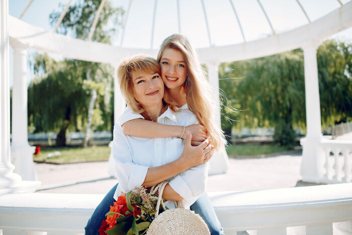 Mother and teenage daughter smiling outdoors, embracing under a white pergola, illustrating advice kids were given. - 29