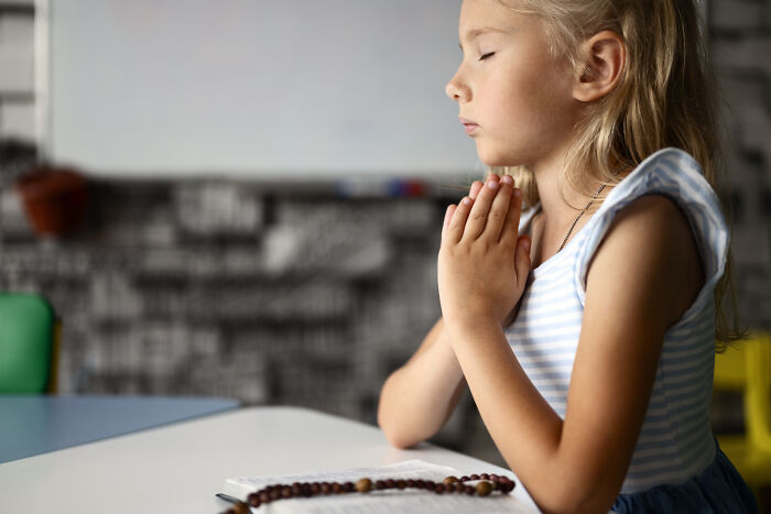 Young girl praying with closed eyes at a table, reflecting on advice kids were given that was manipulation in disguise - 21