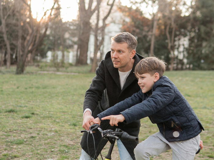 Father teaching son to ride bike outdoors, capturing moments of advice and manipulation in disguise with kids. - 27