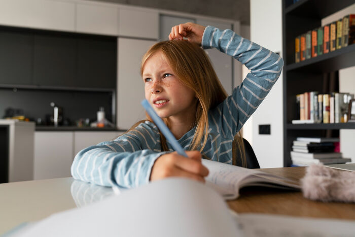Young girl at a desk looking confused while writing, representing kids realizing manipulation in advice later in life. - 28
