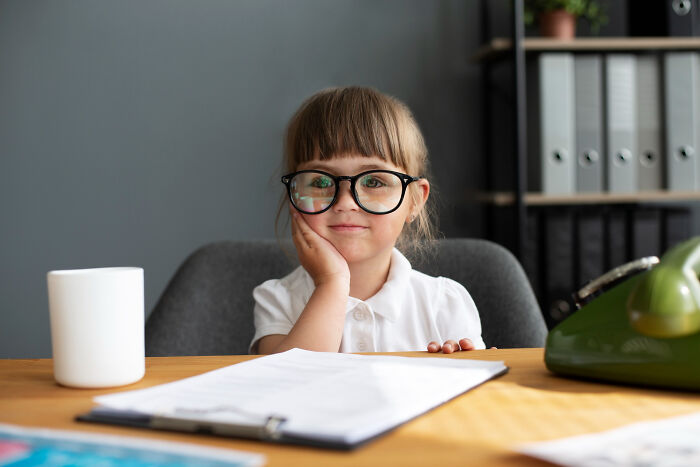 Young girl wearing glasses, sitting at desk with papers, representing advice kids were given and manipulation in disguise. - 16