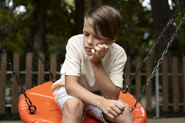Sad boy sitting alone on orange swing at playground reflecting on advice kids were given and manipulation in disguise. - 10