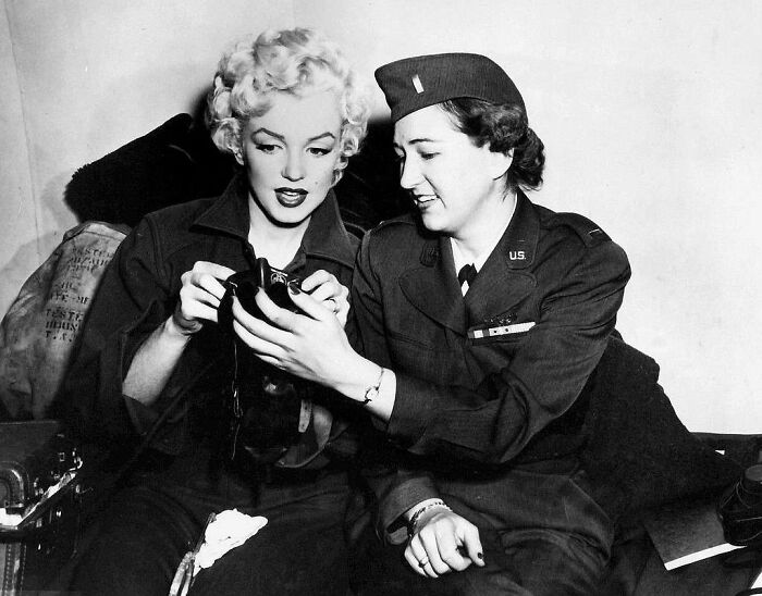 Rare and interesting historical photograph of a woman in military uniform showing a camera to a woman with blonde hair.