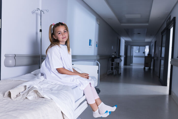 Young girl sitting on a hospital bed in a white gown, symbolizing emotional impact of wife's infidelity in marriage stories.