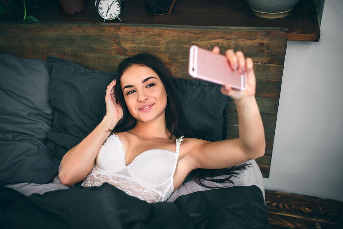 Young woman in lingerie taking a selfie in bed, illustrating themes of wife’s infidelity in troubled marriages.