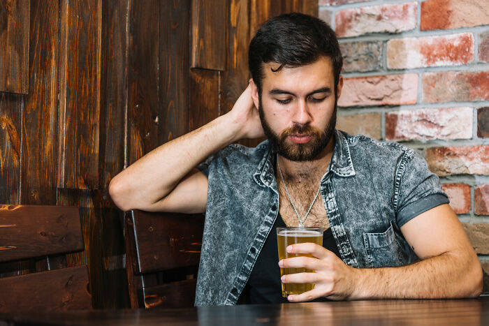 Young man looking sad and thoughtful while holding a drink, reflecting on wife's infidelity and its impact on marriage.