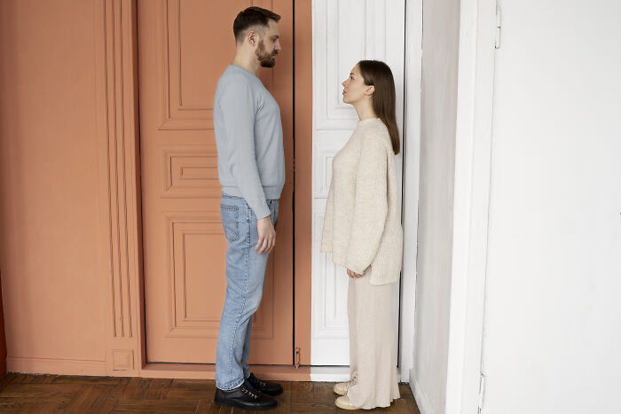 Man and woman standing face to face by closed doors, illustrating tension from wife's infidelity in long-term marriage.