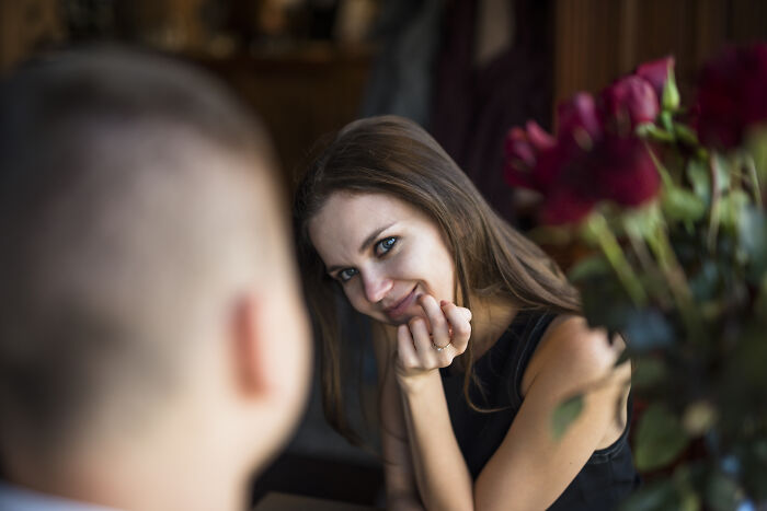 Smiling woman with blue eyes sitting across a man, with roses in the foreground, symbolizing wife's infidelity in marriage.