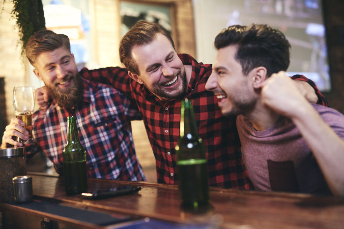 Three men sharing drinks and laughing in a bar, illustrating social moments unrelated to wife's infidelity themes.
