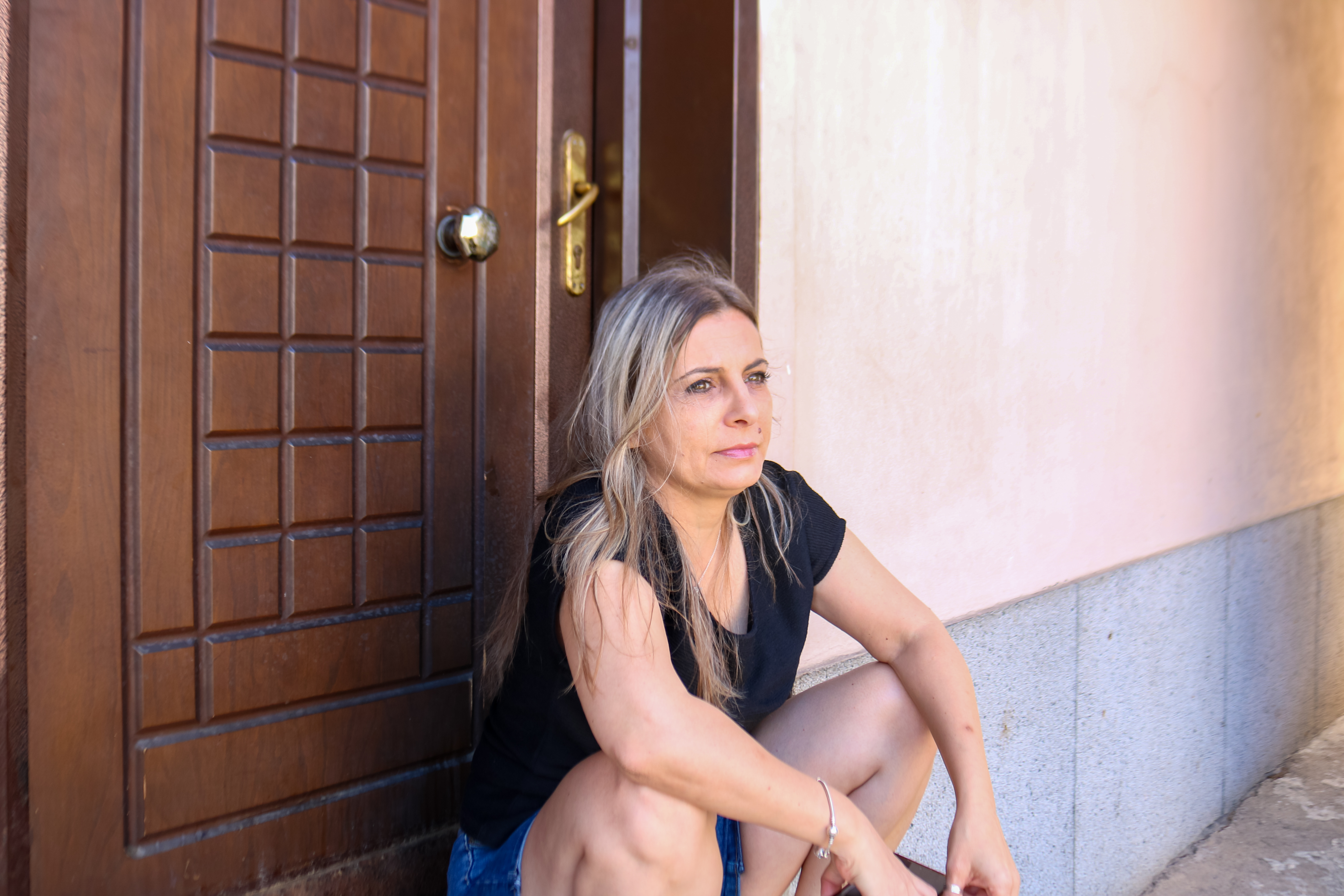 Woman sitting outside a house looking contemplative, illustrating family drama involving inheritance and rent-free living situation.