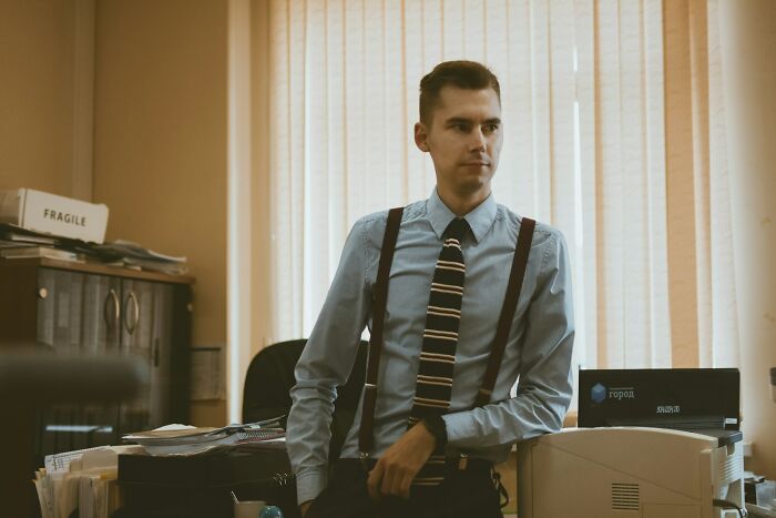 Young man in office wearing suspenders and striped tie, representing themes of pathological liars and deception stories.