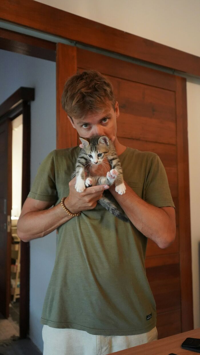 Man in green shirt holding a kitten indoors, illustrating a casual moment related to pathological liars and their stories.