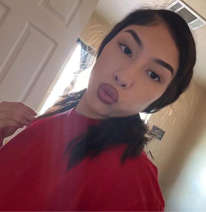 Young woman with dark hair wearing red shirt and posing indoors, related to mass outrage over baby left in car for lip filler. Young woman with dark hair wearing red shirt and posing indoors, related to mass outrage over baby left in car for lip filler.