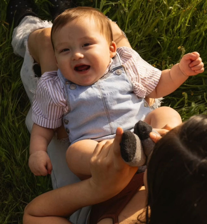 Smiling baby lying on adult’s lap outdoors, illustrating mass outrage over baby left in car incidents. Smiling baby lying on adult’s lap outdoors, illustrating mass outrage over baby left in car incidents.