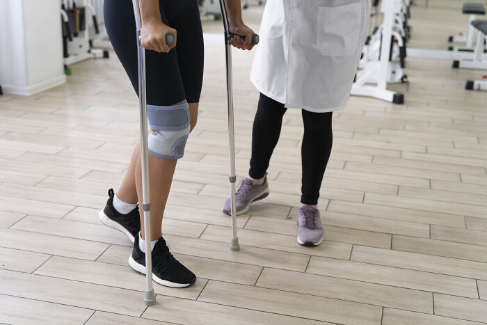 Patient with knee brace using crutches assisted by doctor in a clinical setting illustrating impostor patient stories.