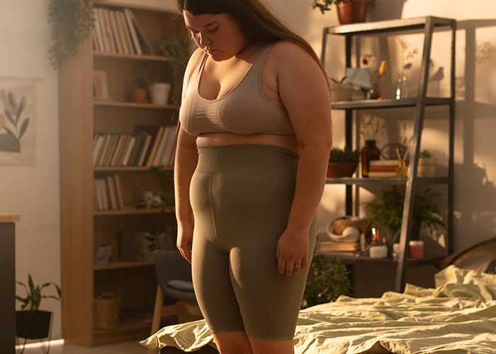 Woman looking down with a sad expression in a bedroom, reflecting on personal experiences of being gaslit by a doctor.