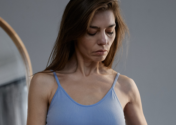 Woman in a blue tank top looking down with a sad expression, illustrating personal experiences of being gaslit by a doctor.