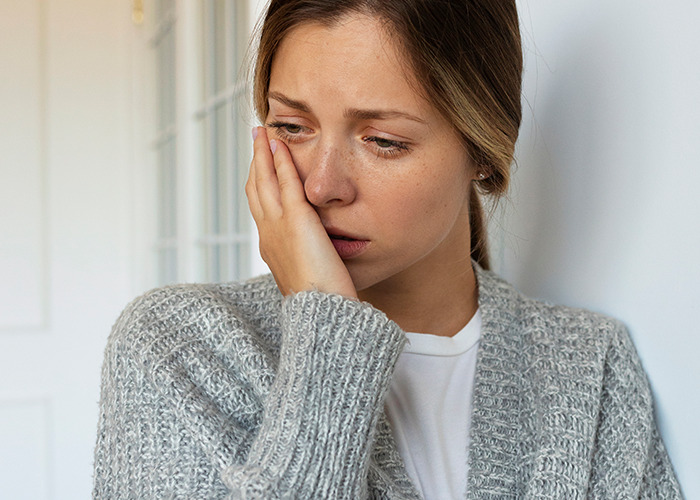 Young woman looking distressed while leaning against a wall, illustrating gaslit by a doctor experience.