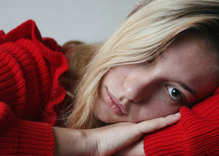 Young woman in a red sweater lying down, reflecting distress from being gaslit by a doctor in a personal experience.