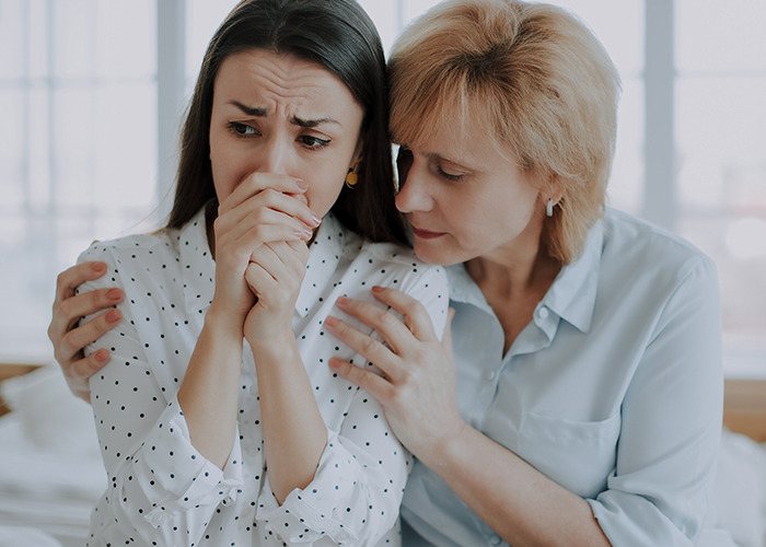 Young woman experiencing emotional distress while another woman comforts her, reflecting gaslit by a doctor experience.