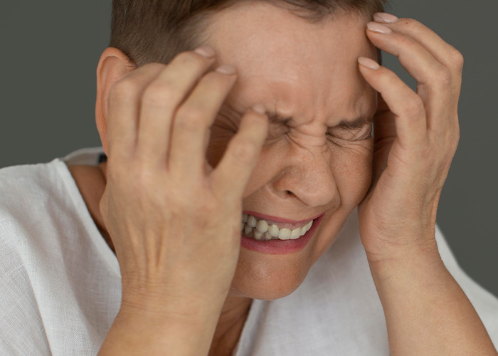 Woman in pain clutching her head, expressing distress related to gaslit experiences by a doctor in a clinical context.