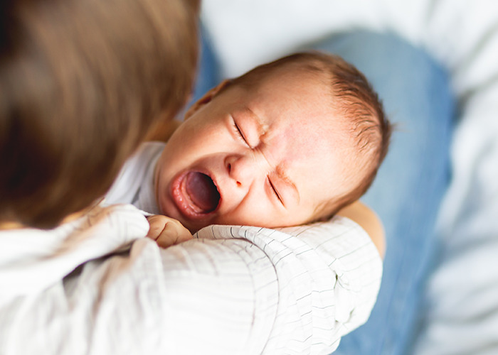 Baby crying in arms of adult, illustrating emotional distress related to experiences of being gaslit by a doctor.