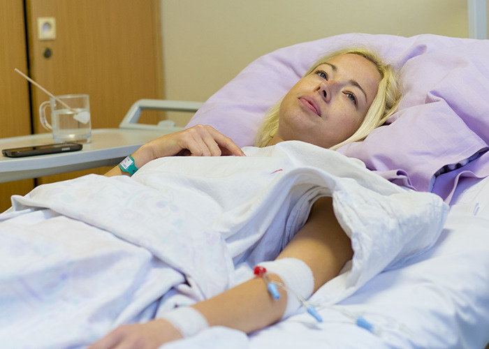 Young woman lying in hospital bed with IV, looking thoughtful and reflective after being gaslit by a doctor.