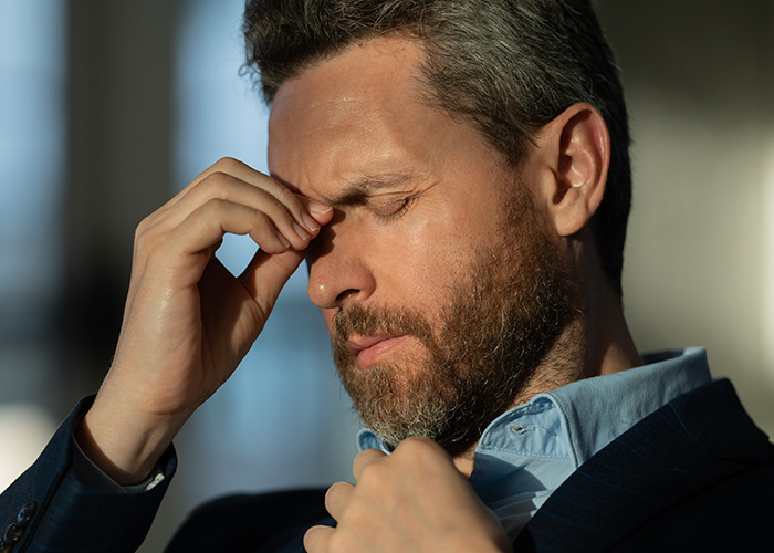 Man with beard and closed eyes showing signs of distress, symbolizing personal experiences of being gaslit by a doctor.
