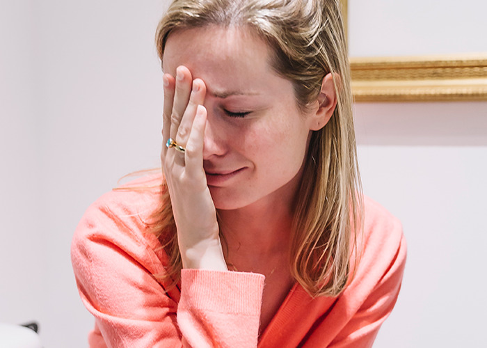 Woman in a coral sweater showing distress and frustration, illustrating experiences of being gaslit by a doctor.